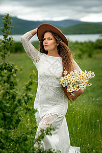 一位身穿白色连衣裙和棕色帽子的中年妇女手里拿着一个篮子 上面放着一大束雏菊 祝贺的野花季节花园生活洋甘菊花束花朵花瓣园艺荒野甘菊图片