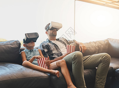 模拟电影体验 一对父女在家里吃着爆米花 戴着虚拟现实耳机看电影图片