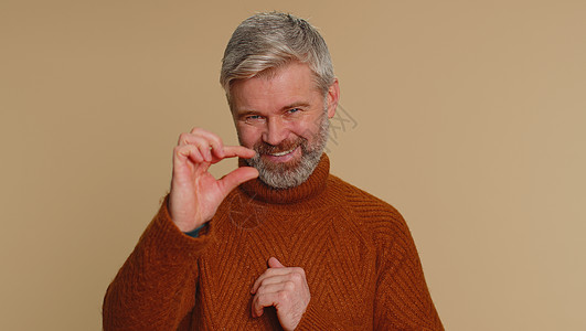 男人用怀疑的笑容展示一点手势 显示最小的标志 测量小尺寸身体男性赞成老年工作室米色背景白发成人厘米图片