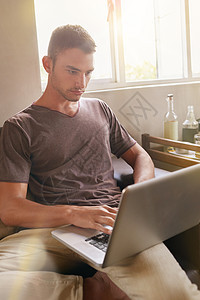 一个英俊的年轻人 在家里沙发上用笔记本电脑打着手提电脑图片