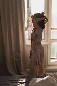 年轻妇女在卧室享受阳光明媚的早晨     觉醒和健康概念房间女性太阳睡衣休息公寓酒店窗帘喜悦窗户图片