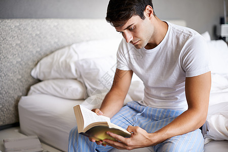 一个英俊的年轻人在床边看书 写着一本书 他从床上出来图片