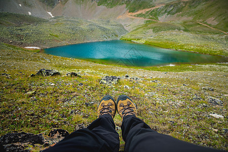 旅行者正躺在山顶高原上 第一人视线 在山绿石湖背景下近距离的双腿图片