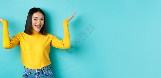 时装和美容概念 时尚美丽的亚洲女孩展示升迁 举起手来微笑 在蓝背景上展示一些东西理发学生广告情感青少年成人快乐交易女性手势图片
