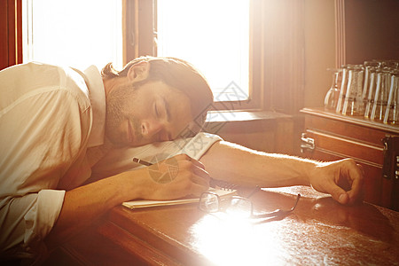 一个英俊的年轻人睡在他的笔记本上 在酒吧里睡觉了头发成人棕色铅笔眼镜记者写作小憩眼睛黑发图片