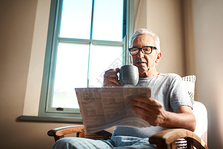 咖啡和新闻是我早上最喜欢的事情 一位老人在家里拿着一杯咖啡坐着看报纸图片