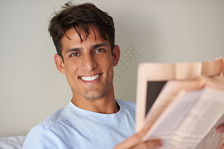 一个英俊的年轻人在他的卧室里看报纸 读着报纸 我很喜欢例行公事图片