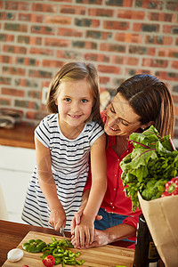 向妈妈学习家庭烹饪秘诀 一个可爱的小女孩和她妈妈在厨房里切菜的画像图片