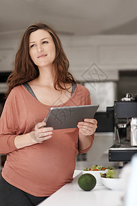 我下顿的晚餐有个好主意 一个孕妇在厨房吃沙拉时 使用她的平板电脑 还用她图片