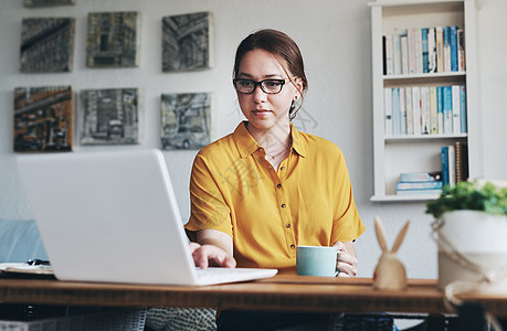一位有吸引力的年轻女商务人士在家中办公室用笔记本电脑 同时还端着咖啡来喝 在她的办公室里图片