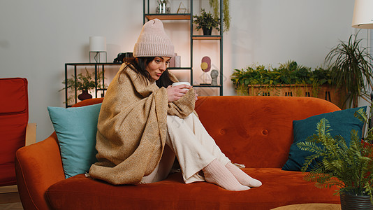 生病 不健康 不健康的妇女戴长格子坐着的帽子 在沙发上喝热茶 从寒冷中颤抖中年呼吸公寓流感格子女士客厅发烧女孩温度图片