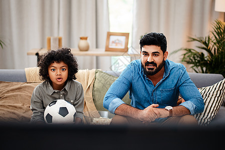比赛现在开始热闹起来 一个可爱的小男孩在家里和他的父亲一起在电视上看足球比赛图片