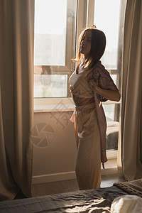 年轻妇女在卧室享受阳光明媚的早晨     觉醒和健康概念女性苏醒房子活力太阳喜悦窗帘窗户酒店睡衣图片