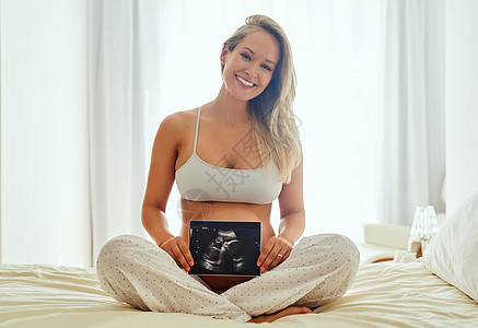一位孕妇在肚子前拿着声波照片 她的腹部被打成一幅动画图片