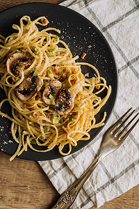 黑盘上放着香菇蘑菇的意大利面 上面撒着奶酪帕尔马干酪和葱 木桌上放着毛巾和叉子盘子香料午餐厨房巾黑色食物桌子面条图片