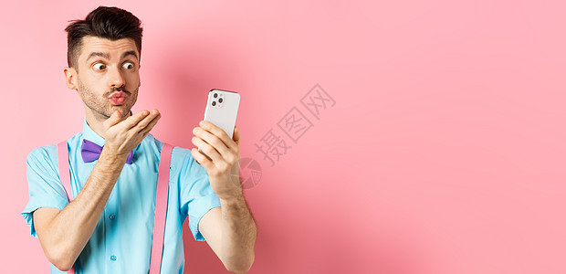 技术概念 有趣的男人在视频聊天时发出空中吻吻 在智能手机相机上吹呼mwah 站在粉红背景上胡子办公室自拍广告快乐工作室电子商务胡图片