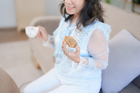 一位亚洲老年妇女在吃零食时喝健康茶的肖像退休女性厨房家庭微笑烹饪水果桌子食品沙发图片