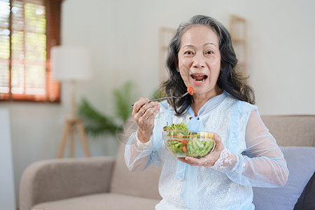 一位年长的亚洲妇女通过吃沙拉来照顾自己的健康烹饪午餐女性祖母厨房微笑桌子退休夫妻沙发图片
