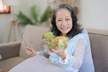 一位年长的亚洲妇女通过吃沙拉来照顾自己的健康厨房退休烹饪夫妻成人食品蔬菜水果老年午餐图片