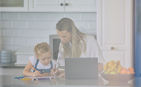 妈妈教孩子在家做作业 轻松的白人母女用笔记本电脑帮助女儿在现代明亮的厨房里画画图片
