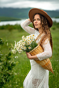 一位身穿白色连衣裙和棕色帽子的中年妇女手里拿着一个篮子 上面放着一大束雏菊 祝贺的野花甘菊天空生活植物花园花瓣洋甘菊荒野花束园艺图片