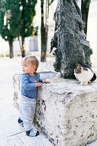 小孩站立 转过侧道 靠近猫坐在的雕塑图片