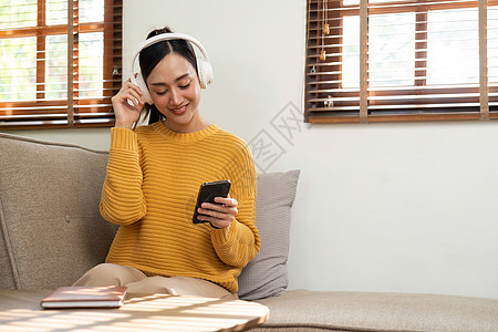 美丽的亚洲妇女 穿着耳机 在家里享受音乐的乐趣歌曲女性房间长椅技术成人快乐闲暇女孩房子图片