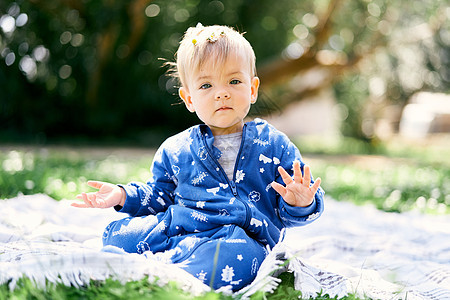 穿着蓝制服的小孩坐在绿草坪上的毯子上 用绿树背景展示他的手掌图片
