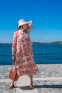 穿着帽子和礼服的女人享受蓝色的海洋和夏天 欢迎夏天房间栏杆女性乐趣女士海岸裙子旅行卷曲微笑图片