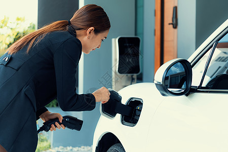 进步女性在家庭充电站为她的EV车补充补给充电器住宅车辆排放驾驶电池环境燃料充值电动车图片