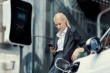 进步女商务人士 有模拟智能手机 在充电站与EV活力公寓充值人士商务车站技术汽车运输城市图片