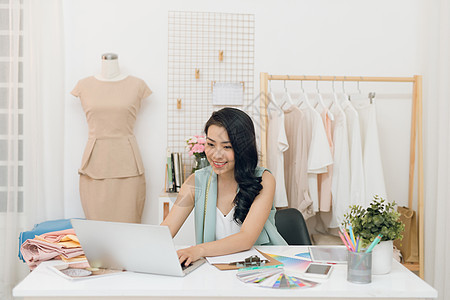年轻的亚洲时装设计师肖像 坐在工作间笔记本电脑前的办公桌上职业企业家女性裙子工作室女裁缝创造力人体幸福织物图片