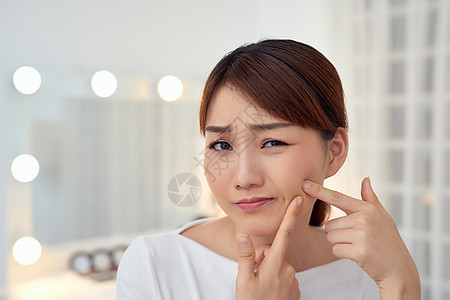 年轻的亚裔女子不快乐触摸她的皮肤手指镜子疙瘩女孩粉刺卫生女士反射护理图片