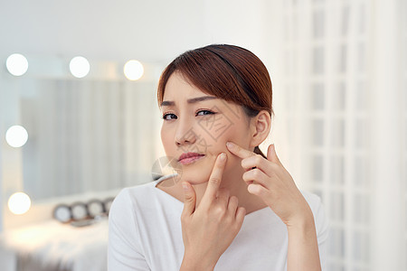 年轻的亚裔女子不快乐触摸她的皮肤女孩女士手指卫生疙瘩护理反射粉刺镜子图片