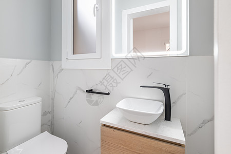 有厕所和设计师的小浴室用黑色水龙头装在小虚荣上 墙壁由白色天然大理石砖制成 广场镜子用荧光灯照亮图片