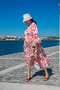 穿着帽子和礼服的女人享受蓝色的海洋和夏天 欢迎夏天天空女士头发裙子阳光旅游成人乐趣房间自由图片