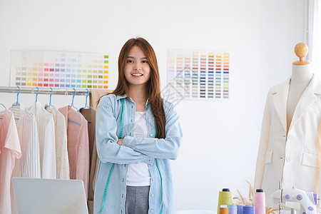 一个年轻的年轻女性时装设计师 站在怀抱自信的臂膀上 看着她设计室里的摄影机女裁缝商城人士造型纺织品企业家业主网上购物职业创造力图片