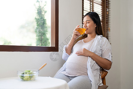 在家坐着吃沙拉和橙汁的怀孕年轻孕妇快乐图片