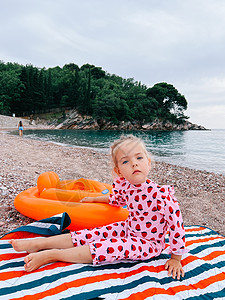 小女孩坐在沙滩上的毯子上 手放在一个充气的戒指上图片