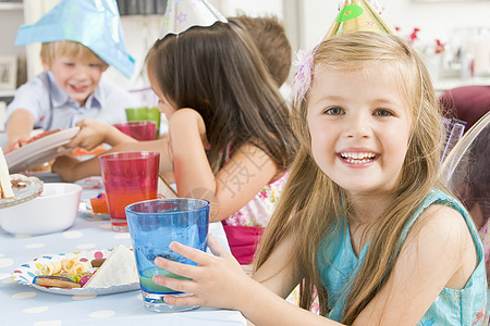 参加派对的年轻女孩坐在餐桌边吃着微笑的食物孩子生日果汁橙汁相机女性桌子孩子们水平图片