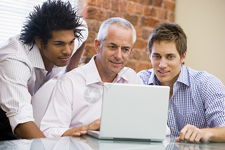 三名在办公室的商务人士笑着看笔记本电脑图片
