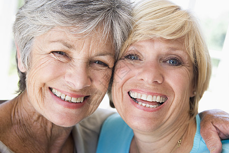 两个在客厅的妇女微笑着笑着退休相机最好的朋友朋友们女性拥抱亲密感团结两个人友谊图片