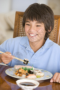 饭厅的年轻男孩在吃中国食物时微笑着笑小男孩刀具用具寿司健康饮食餐具孩子筷子美食一个男孩图片