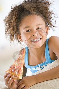 年轻女孩在客厅里笑着吃披萨片儿童倾斜孩子食物偏移混血儿视角一个女孩微笑送货图片
