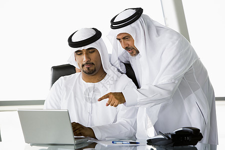 两名在职商务人士指着笔记本电脑一代桌子通讯窗户讨论生意人男士伙伴婴儿同事图片