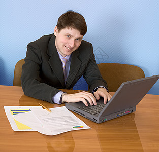 商务人士用笔记本电脑坐在桌子上人士男性工作商业套装蓝色笑脸按钮夹克办公室图片