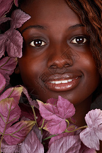 美丽的非洲女孩爆头微笑女士棕色紫色树叶黑色背景图片