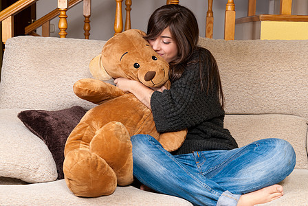 年轻女人坐在沙发上 拥抱泰迪熊图片