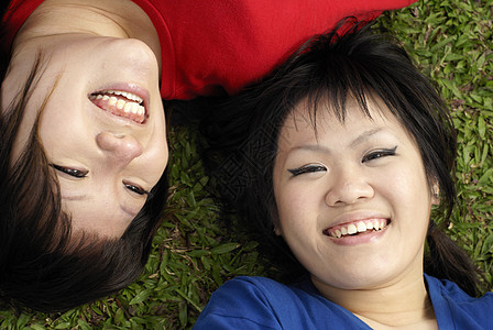 两个快乐的亚洲少女 躺在草地肖像上 穿着红蓝衣服乐趣女孩们青少年蓝色幸福微笑红色图片