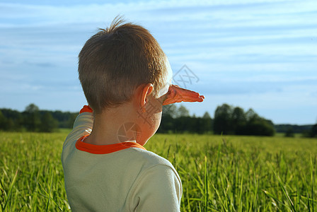 快乐的年轻男孩看着地平线 在绿田上做梦图片